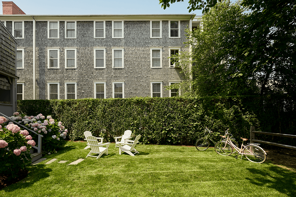 A backyard with two white chairs, bicycles, and pink hydrangeas next to a wooden building.