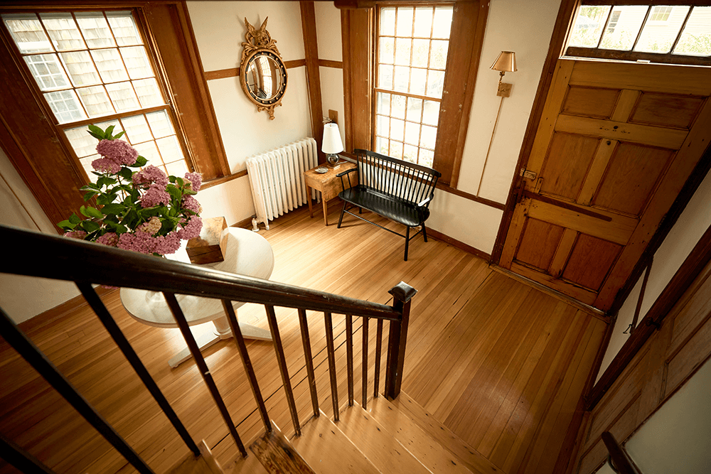 Foyer of a historic, old house, viewed looking down staircase, looking at back of front door with a bouquet of hydrangeas on a side table nearby.