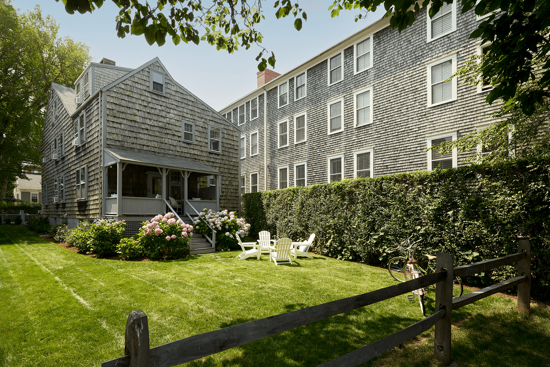 Adirondack chairs on a green backyard lawn with hydrangea bushes on either side of a back porch of a historic home.